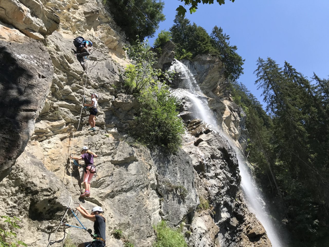 Ein Wasserfall mit zwei Personen die einen Klettersteig absolvieren.